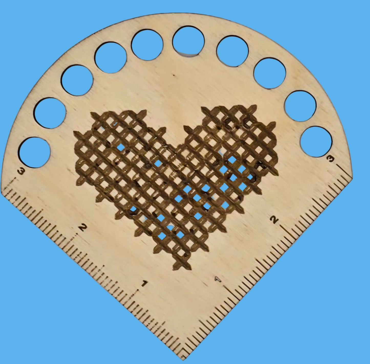 A wooden thread keeper with a heart shape and measurement markings, featuring a needle and a heart-shaped pattern burnt into the wood.