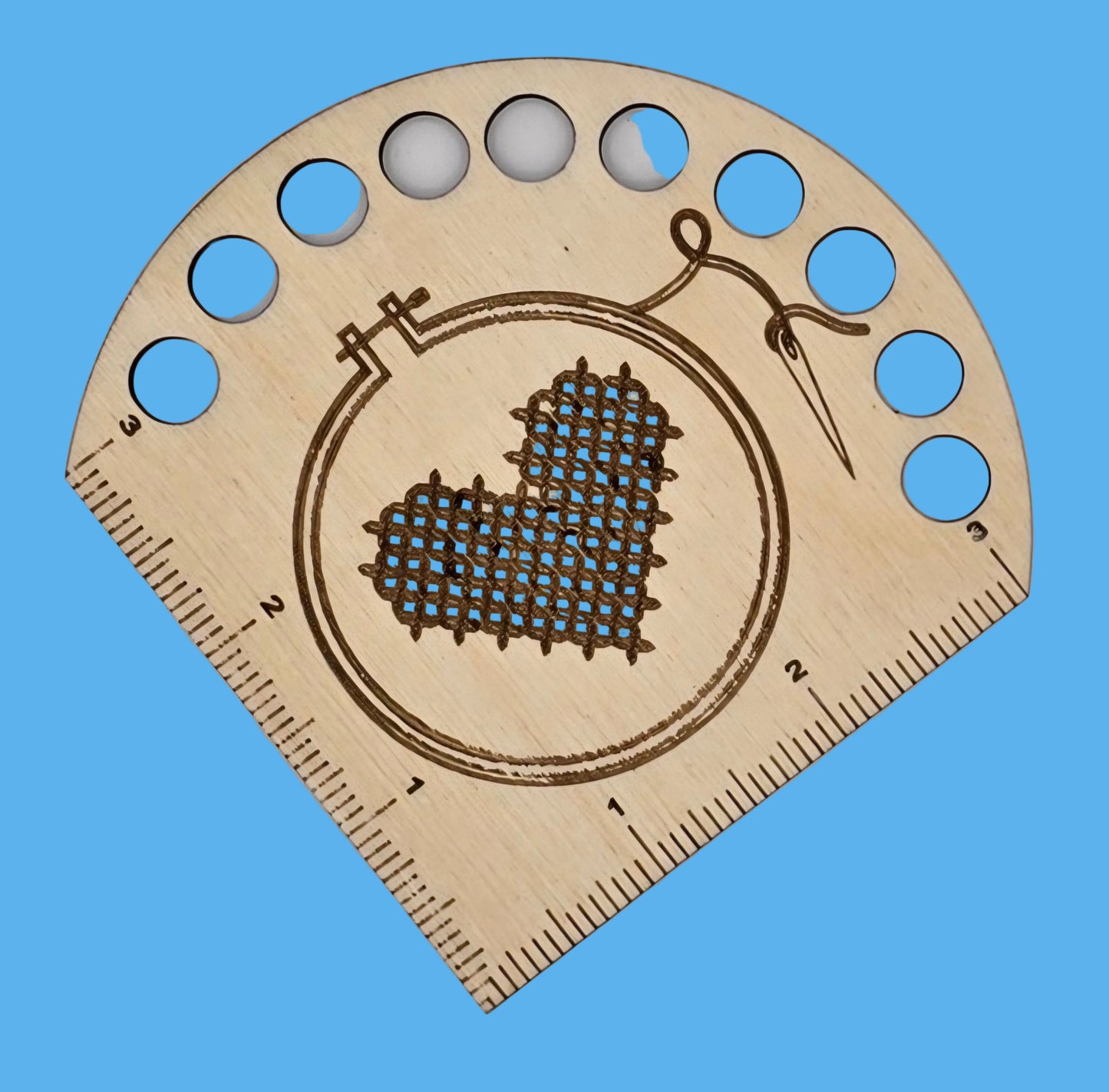 A wooden thread keeper with heart and hoop design, featuring measurement markings and holes for thread organization.