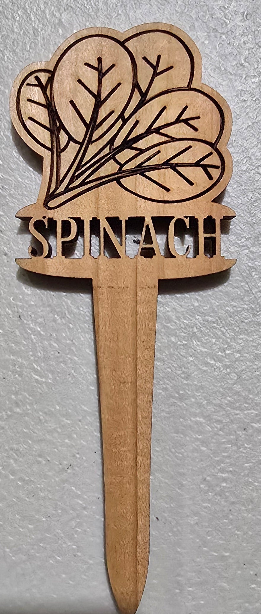 Wooden Spinach plant marker design on a white surface