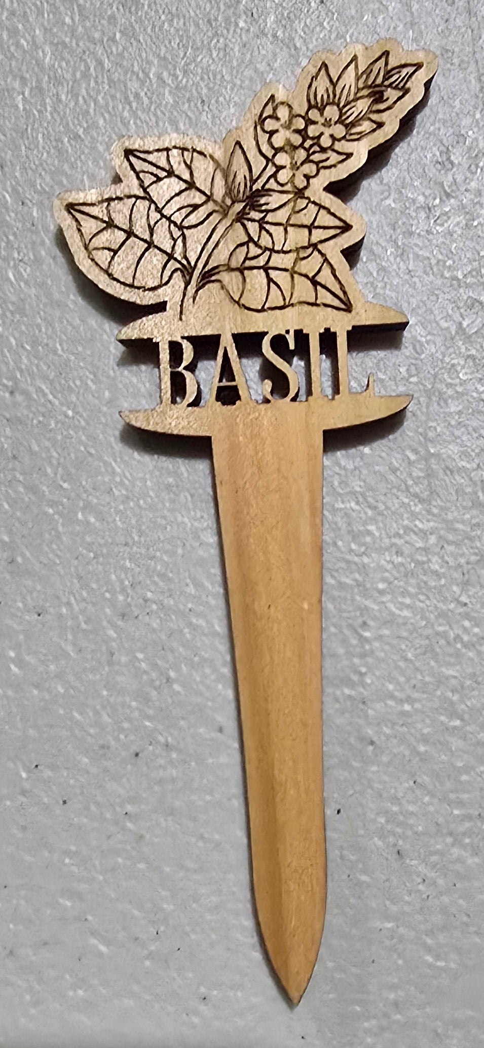 Wooden basil plant marker with intricate design on a gray surface