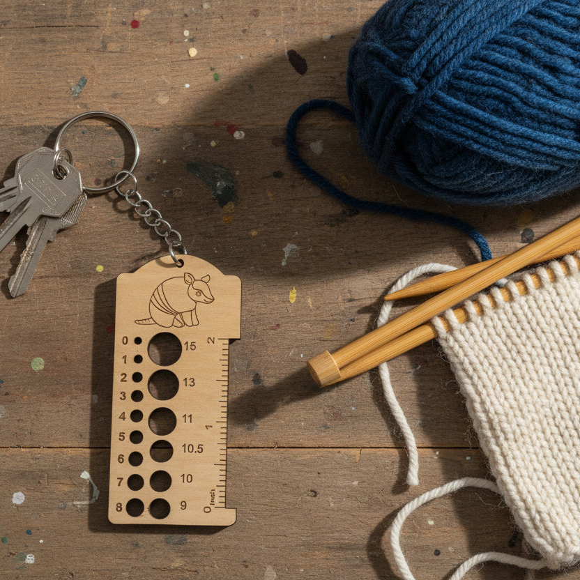 Wooden armadillo knitting needle gauge keychain with yarn and needles on wood surface
