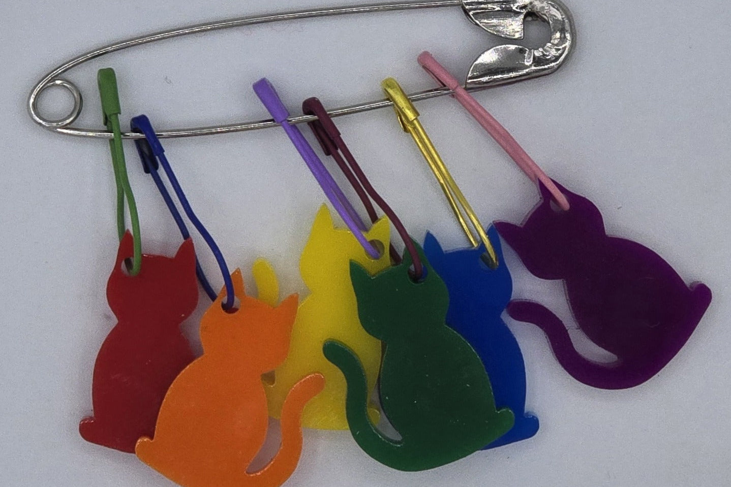 Colorful cat-shaped charms on a metal safety pin against a white background