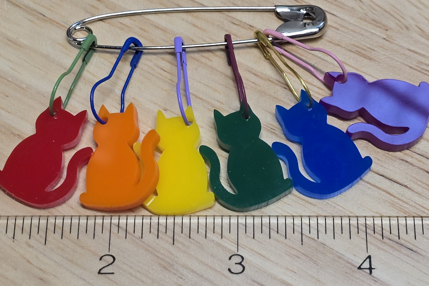 Colorful cat-shaped keychains on a wooden surface with a ruler for scale.