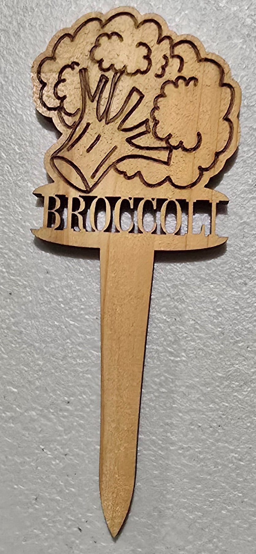 Wooden toothpick with laser-cut broccoli design on a light gray background