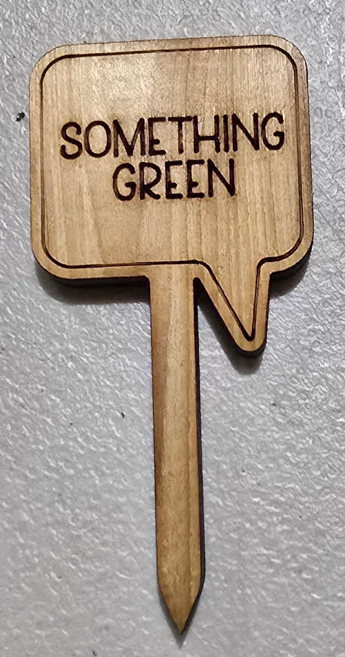Wooden arrow-shaped sign with 'Something Green' text on a gray background