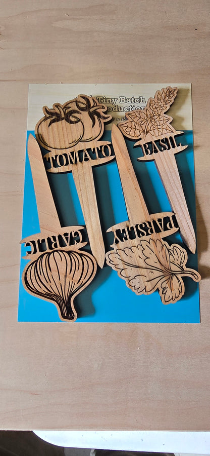 Wooden garden markers with plant names on a blue card against a cardboard background
