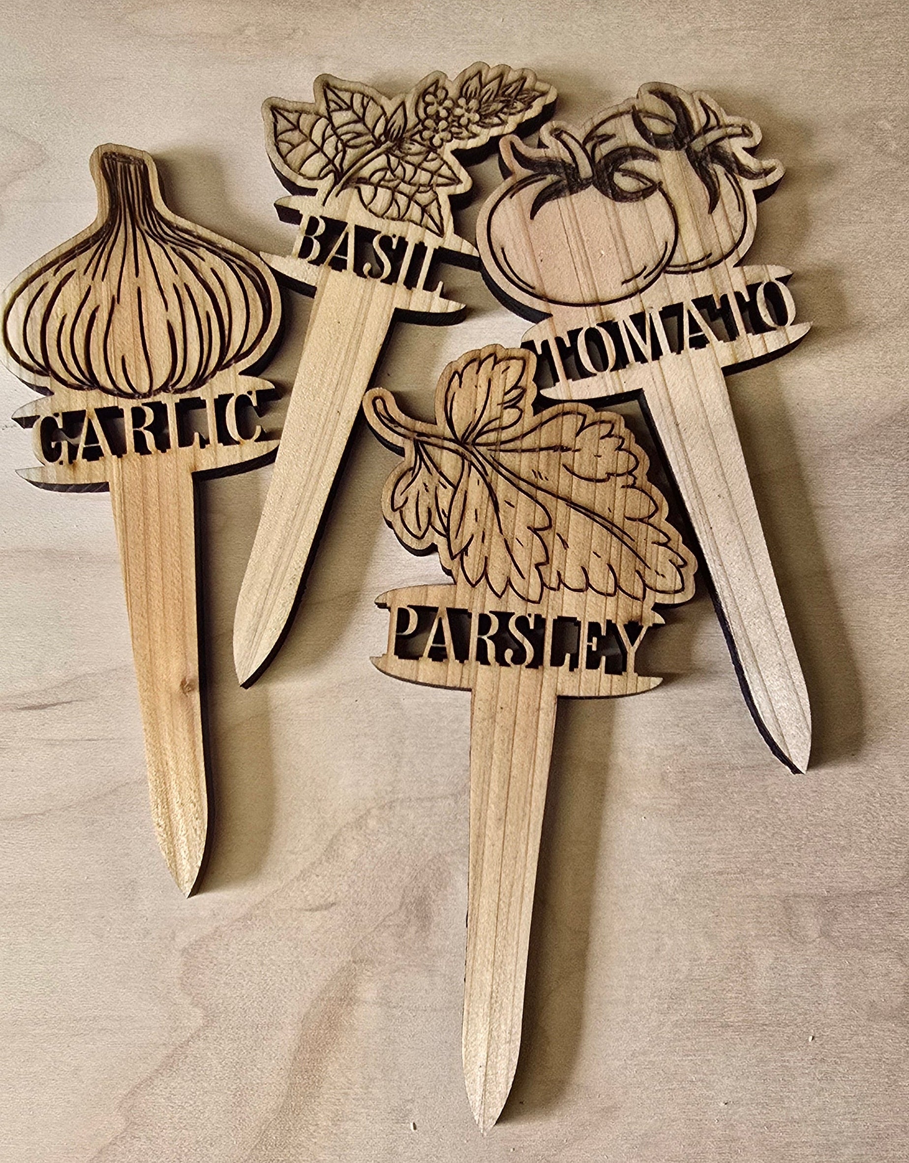 Wooden plant markers with laser-cut designs and text on a wooden surface.