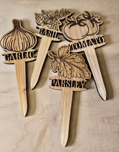 Wooden plant markers with laser-cut designs and text on a wooden surface.