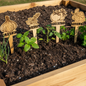 Wooden garden markers with plant names in a raised garden bed.