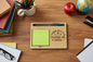 Wooden tray with green sticky notes, pen, and 'Thank you for helping me grow' text on a wooden desk with books, an apple, and a globe.