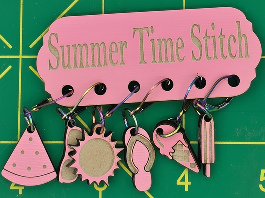 Pink needle minder with summer-themed charms on a green grid background